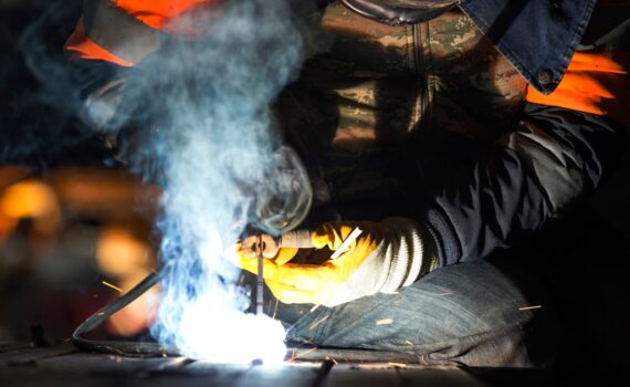 The welder is welding with shielded metal arc welding, manual metal arc welding or stick welding. Electric current is used to strike an arc between the base material and consumable electrode rod.