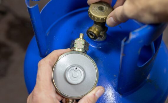 Regulator for propane-butane gas cylinder and accessories on a wooden workshop table. Gas accessories in the workshop. Dark background.