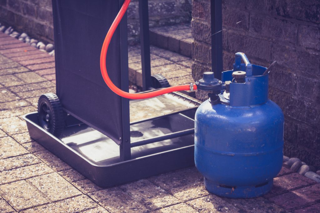 Large blue gas canister attatched to a portable barbecue on wheels in a domestic garden
