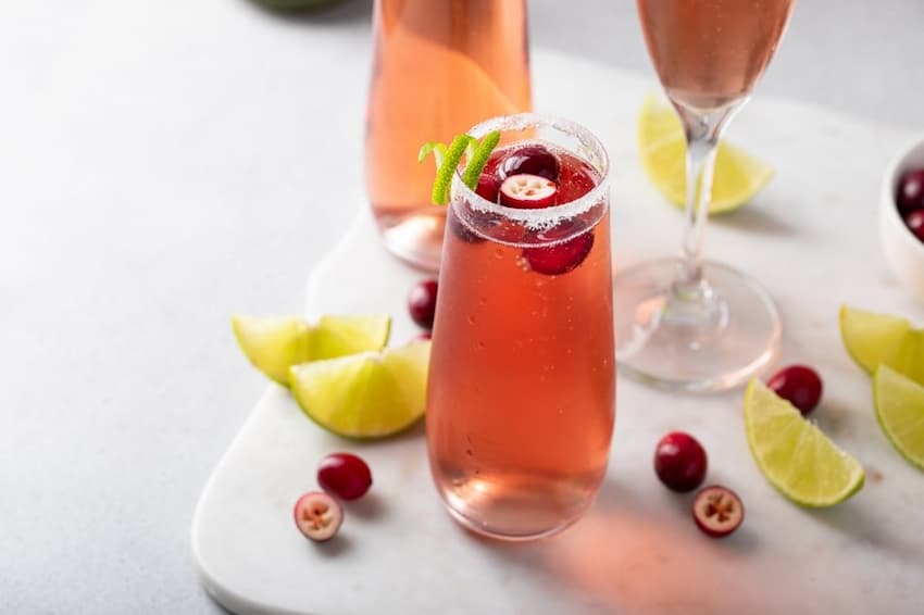 A glass of pink drink with cranberries and limes